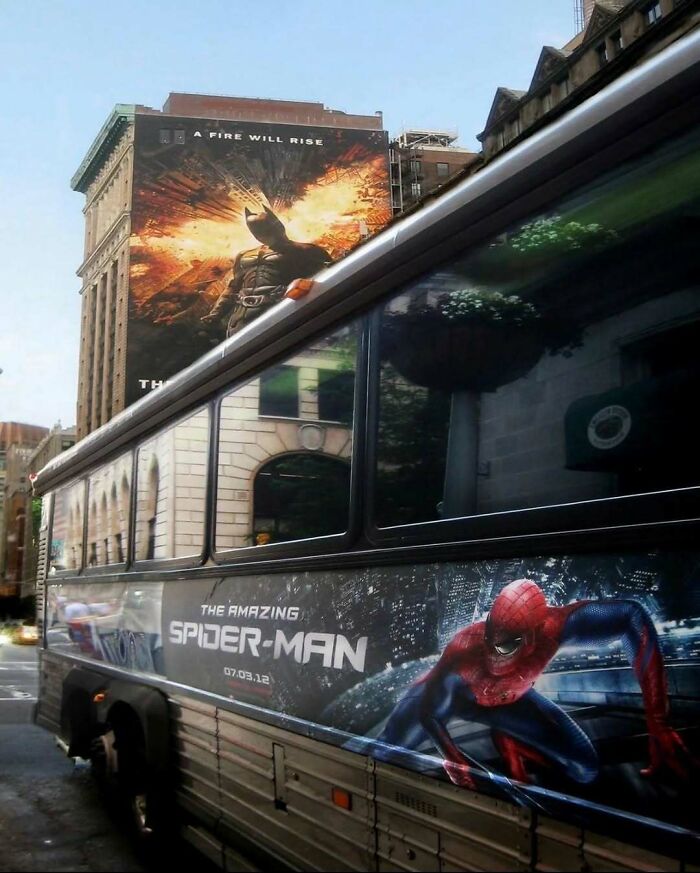 A city street with a Spider-Man bus ad passing under a Batman billboard in hilarious pics.