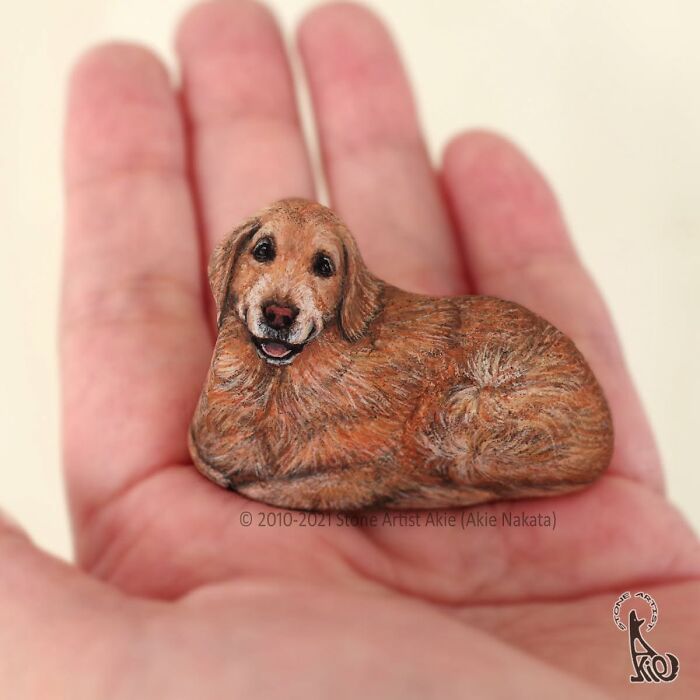 Stone art of a smiling golden retriever dog held in a palm