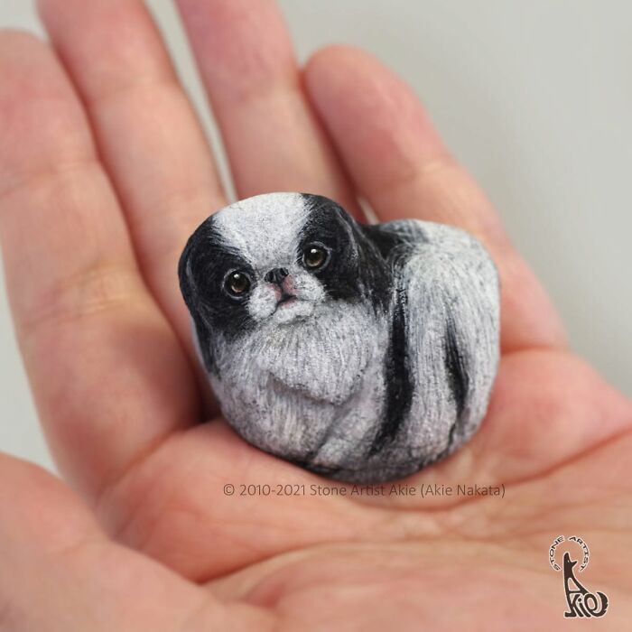 Hand holding a small black and white dog painted stone with fine detail