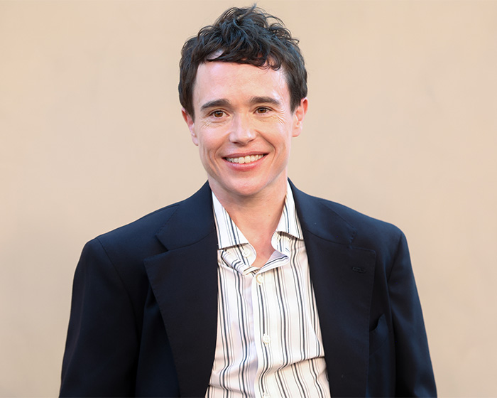 Actor Elliot Page smiling in a suit, highlighted among prominent trans actors in Hollywood.