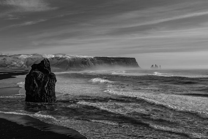 Large basalt rock formation standing in the crashing surf along a black sand beach in Iceland.