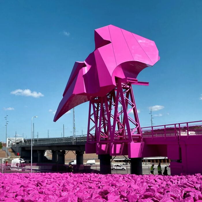 A bright pink public art sculpture integrated into a bridge over a rocky ground painted entirely in pink.