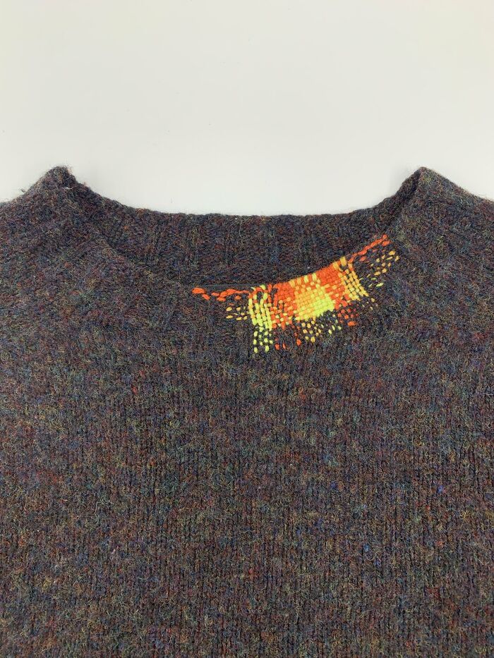Colorful woven repair on a dark sweater collar showing how a little creativity saves money