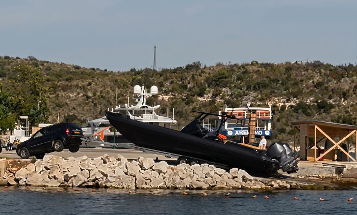 Black SUV with front wheels lifted off the ground by a heavy speed boat on a trailer, a bad case of towing gone wrong.