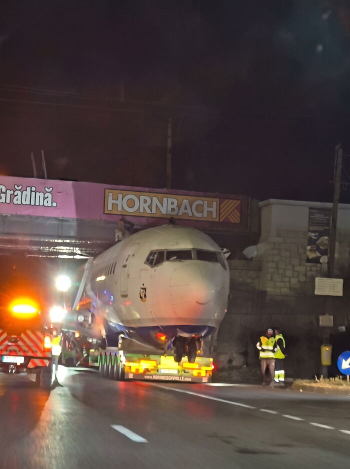 Large airplane fuselage stuck while being transported under an overpass at night, showing heavy transport towing gone wrong.