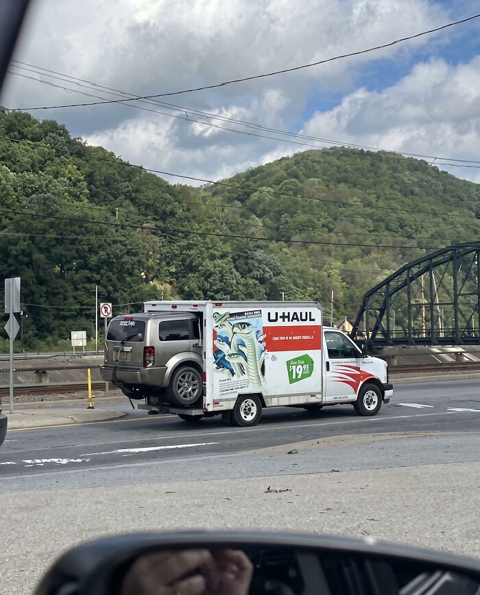 An SUV dangerously loaded inside the back of a moving U-Haul truck showing towing gone wrong.