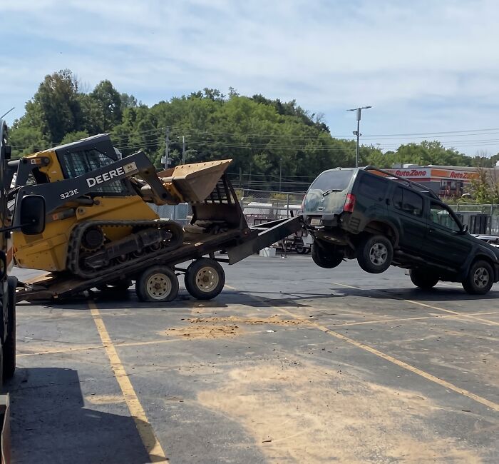A heavy construction vehicle loading onto a trailer, showing towing gone wrong in a parking lot.