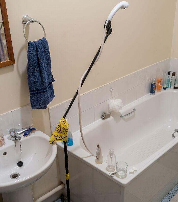 A shower head crudely taped to a metal stand next to a bathtub, representing a makeshift way to renovate their homes.