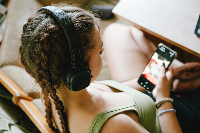 A girl with braided hair and headphones sitting down, looking at her smartphone where she has viral followers A girl with braided hair and headphones sitting down, looking at her smartphone where she has viral followers