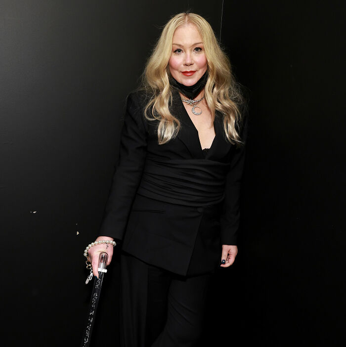 Christina Applegate posing in a black suit holding a cane.