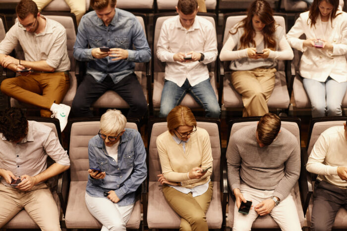 A group of people sitting in rows of theater seats, all looking down at their smartphones, raising concerns A group of people sitting in rows of theater seats, all looking down at their smartphones, raising concerns