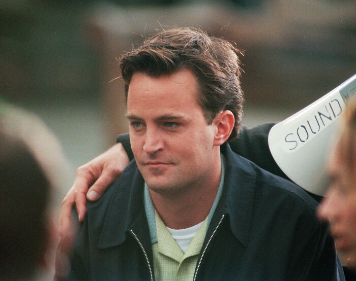 A close-up portrait of late actor Matthew Perry looking thoughtful during a filming set.