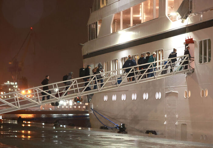 Passengers with luggage walking up the gangway to board a permanent cruise ship at night Passengers with luggage walking up the gangway to board a permanent cruise ship at night
