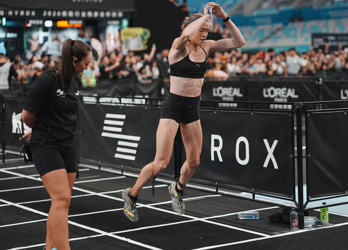 A female HYROX athlete performing burpee broad jumps during an intense workout competition