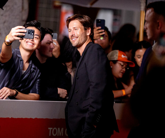 Hollywood star Glen Powell smiling and posing with fans at a red carpet event.