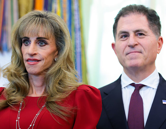 Woman in red dress standing next to man in suit during an official event Woman in red dress standing next to man in suit during an official event