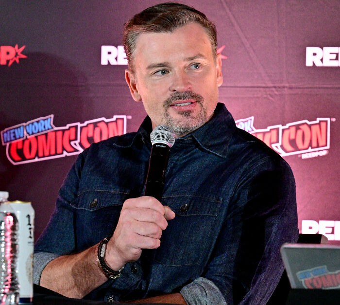 TV star Tom Welling speaking into a microphone at New York Comic Con backdrop