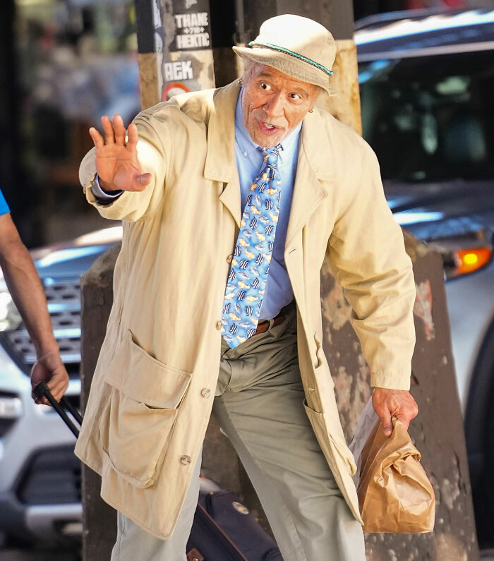 Unrecognizable Hollywood superstar in makeup and costume holding a paper bag on a city street.