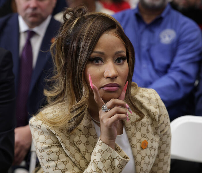 Nicki Minaj resting her chin on her hand in a beige patterned suit at a Trump rally. Nicki Minaj resting her chin on her hand in a beige patterned suit at a Trump rally.
