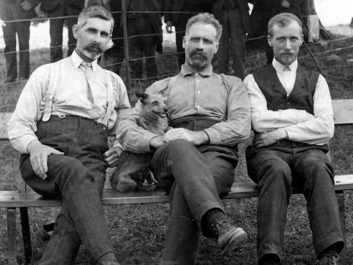 Vintage black and white photo of three men with a dog sitting together, representing historic cults
