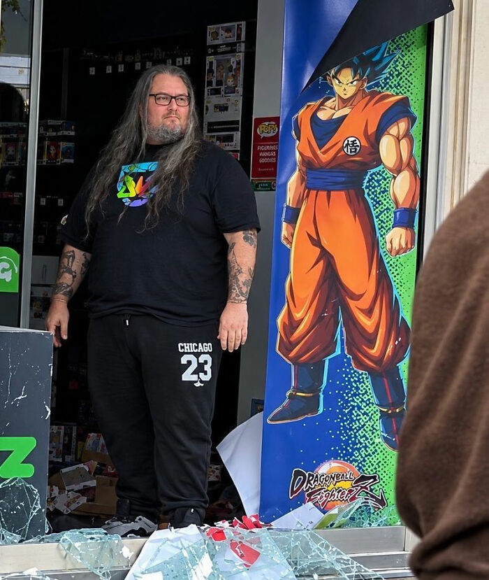 Shopkeeper standing next to Dragon Ball Fighter Z poster in store with broken glass