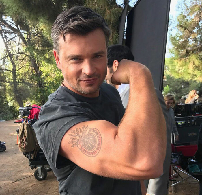 TV star Tom Welling smiling and flexing his bicep on set