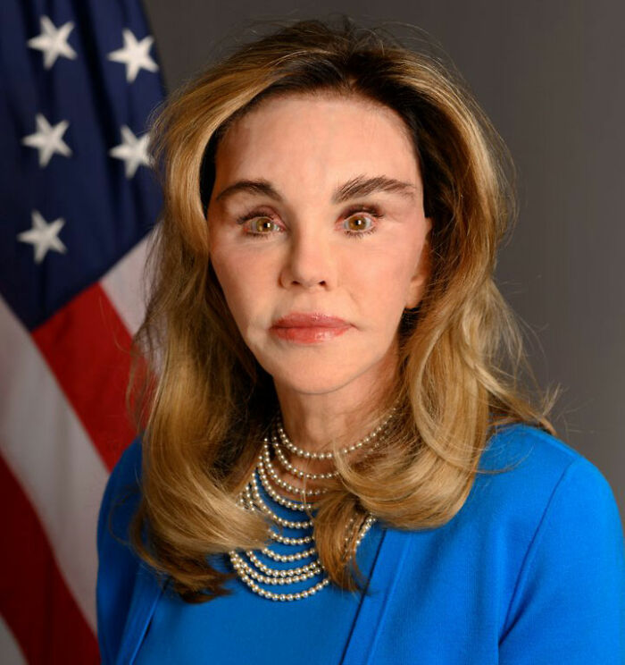 Woman in blue dress with pearls standing in front of American flag in official portrait Woman in blue dress with pearls standing in front of American flag in official portrait