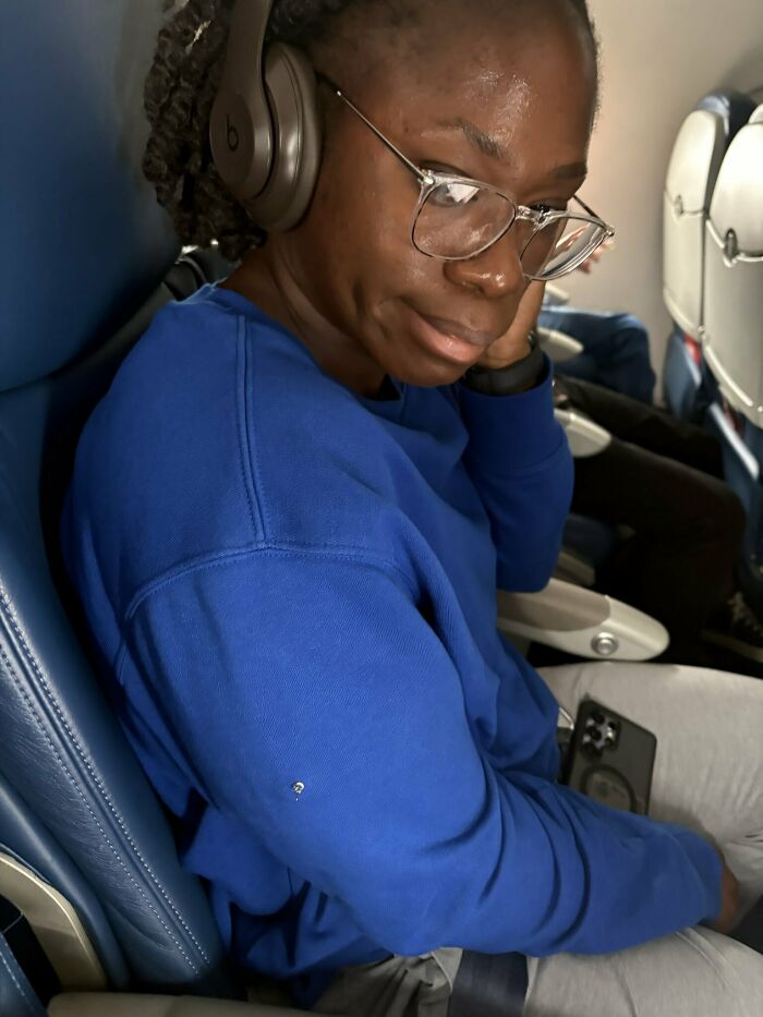 Woman seated on airplane wearing a blue sweatshirt with an earring attached to her sleeve Woman seated on airplane wearing a blue sweatshirt with an earring attached to her sleeve