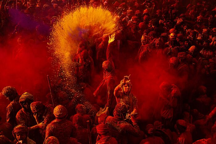 Large crowd covered in vibrant red and orange powder during festival photo awards