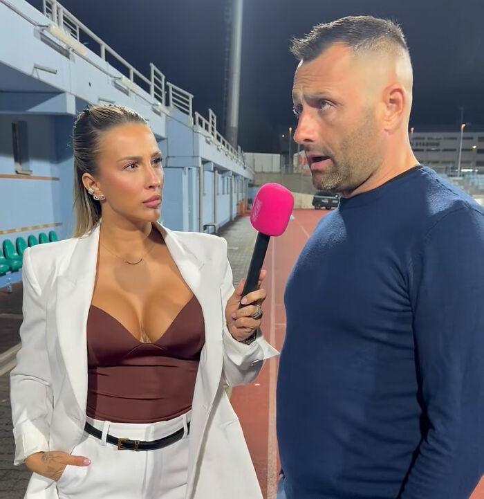 Football coach avoiding eye contact during interview with female reporter holding pink microphone