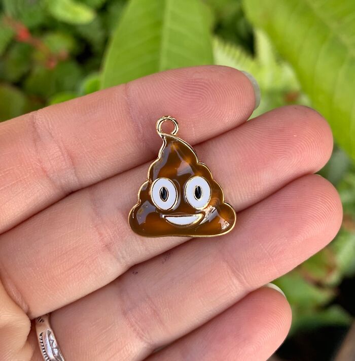 A small smiling p**p emoji charm held in a hand