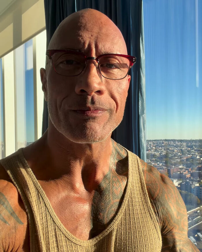 Close-up of Hollywood superstar Dwayne Johnson taking a selfie indoors wearing glasses.