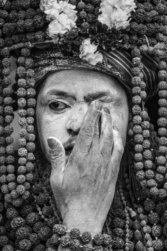 A monochrome portrait photo of a sadhu with ash on his face covering one eye, displaying a unique human expression.