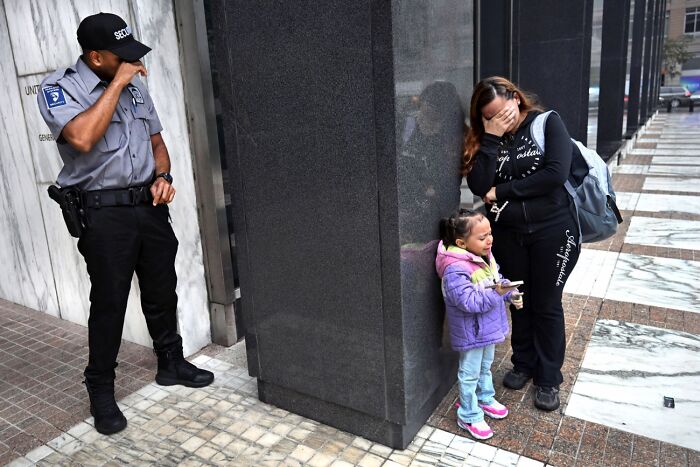 Security guard standing near distressed woman and child on city sidewalk, best pics 2026 Siena International Photo Awards