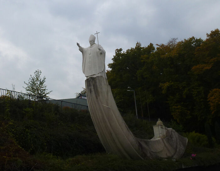 Bizarre public art showing a tall white statue of a Pope standing on a giant curved structure