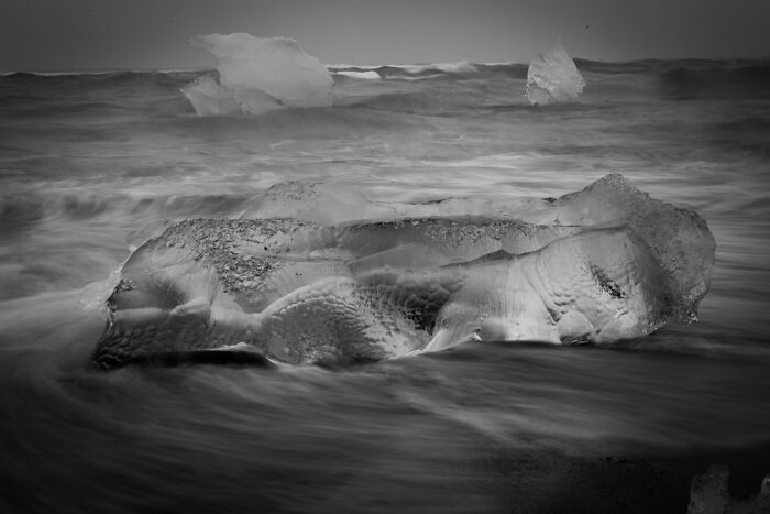 Chunks of glacial ice washed ashore on a black sand beach in Iceland surrounded by ocean waves.