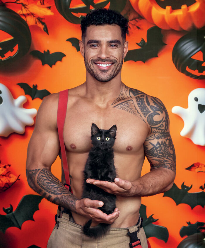 Tattooed firefighter holding a black cat with Halloween decor in Australian calendar