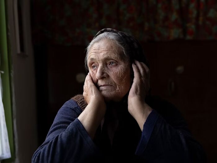 An elderly woman looks out a window with a pensive look, showcasing the beauty of human expression in portrait photos.