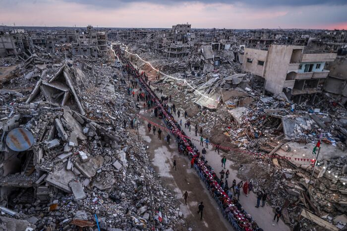 Long line of people walking through war-torn destroyed buildings showing urban devastation