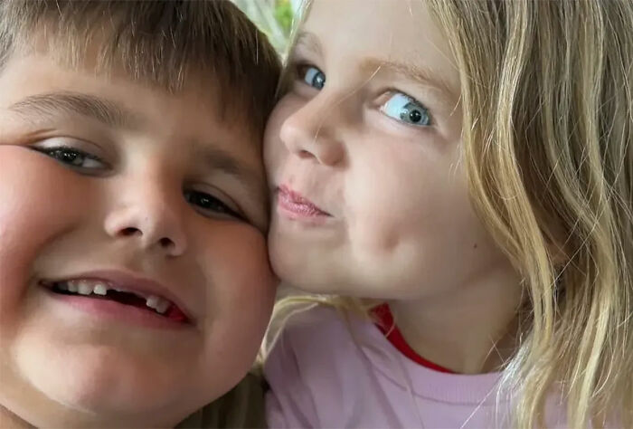 Close up photo of 2 young children smiling together cheek to cheek.