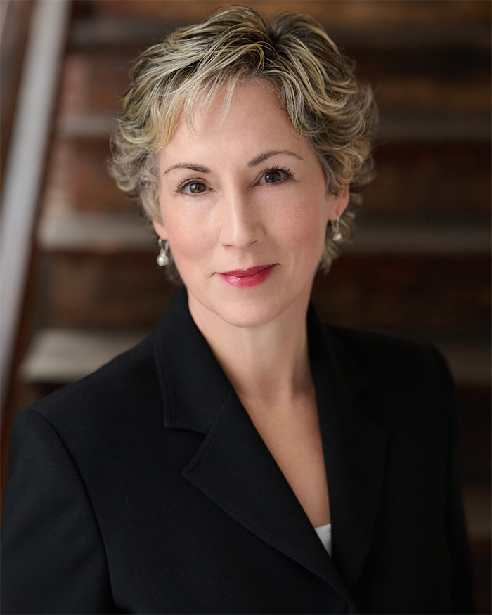 Professional headshot of a female expert with short blonde hair wearing a black blazer.