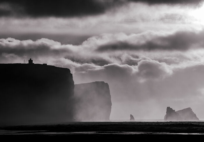 Misty coastal cliffs and sea stacks along the black sand coast of Iceland in black and white.
