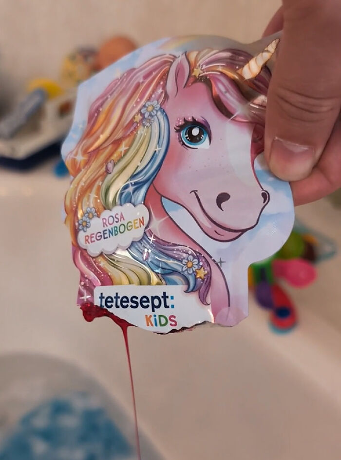 A hand holding absurd products including bath soap in a unicorn packet leaking red liquid.