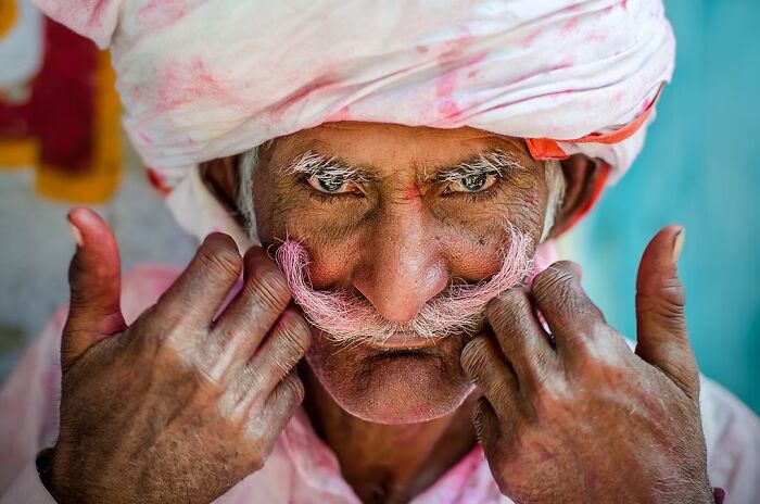Vibrant portrait photo of a man adjusting his pink-dyed mustache, capturing a spirited human expression.