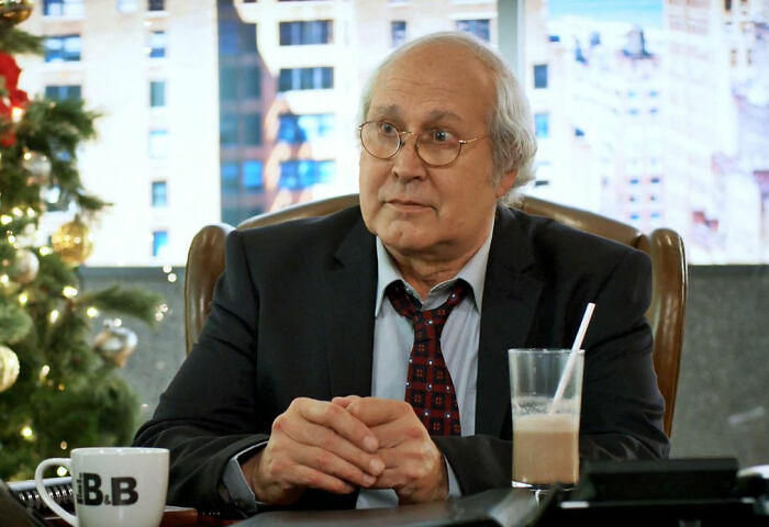 Actor Chevy Chase sitting at a desk, one of the stars who got in the way of their own success.