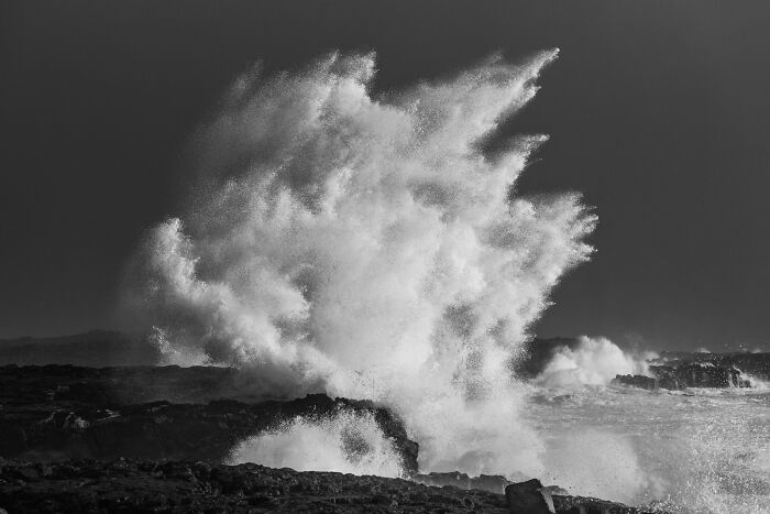 Powerful ocean waves exploding into white spray over dark rocks along a black sand Iceland coastline.