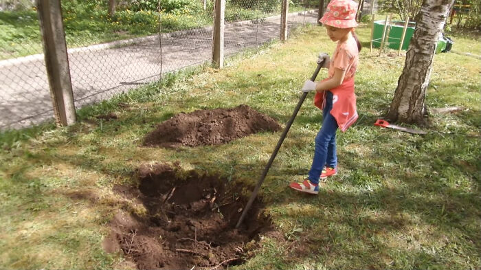 Young child digging a hole in the yard with a shovel while trick-or-treating