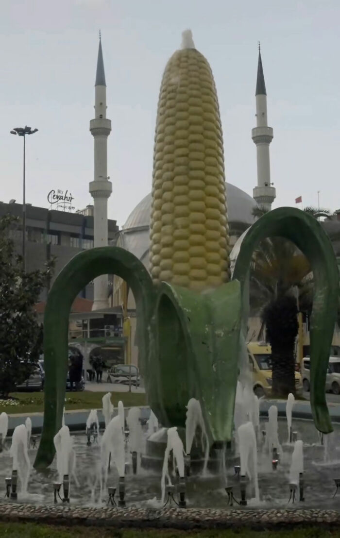 A giant corn on the cob fountain as public art with a mosque in the background.