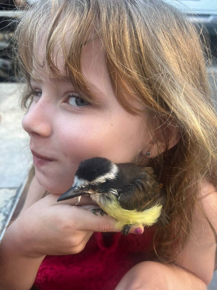 A young girl holding a small bird close to her cheek