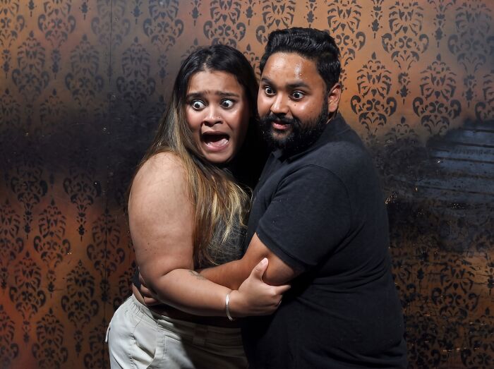 Terrified couple holding each other in fear with wide eyes in funny haunted house photos.